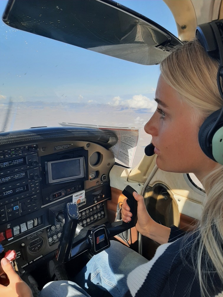 Maddi flying a Piper aircraft, wearing a headset and focusing on the flight controls
